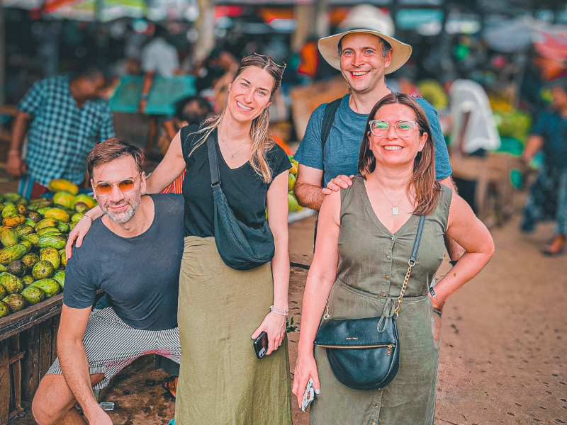 Group of happy tourists posing with a local vendor at a bustling morning market on a Colombo food tour