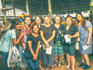 A large group of female travelers holding baskets and selecting ingredients at a local Colombo market during a Sri Lanka cooking class with Rustic Colombo cooking class.