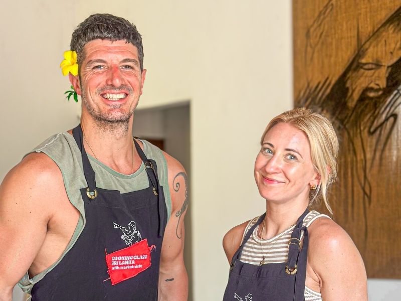 Couple smiling in Sri Lankan cooking class aprons with flowers in their hair, ready for hands-on Negombo Cooking Class after market tour