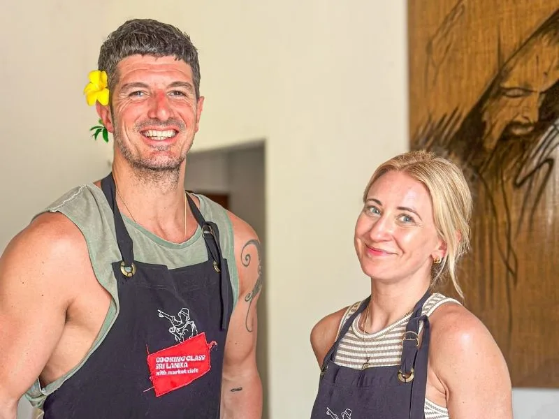 Couple smiling in Sri Lankan cooking class aprons with flowers in their hair, ready for hands-on Negombo Cooking Class after market tour
